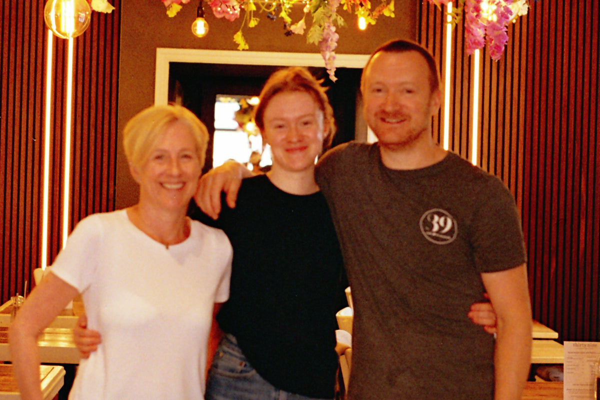 Three people standing together with a decorated floral arch in the background