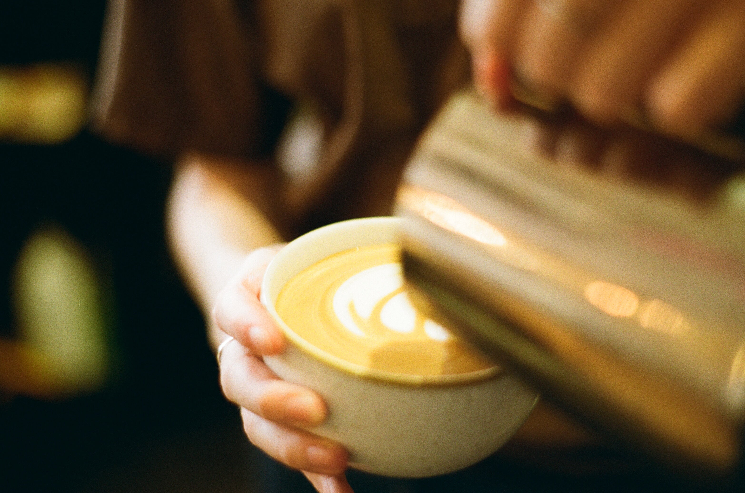 A hand holding a ceramic coffee cup pouring milk in with a blurry background