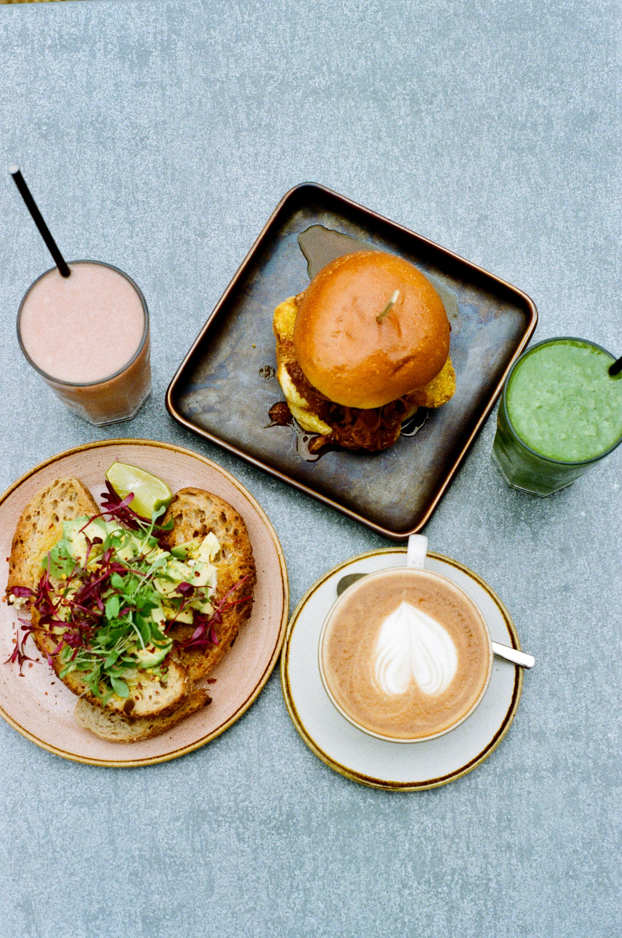Assorted food items including a burger, sandwich, and drinks on a textured surface