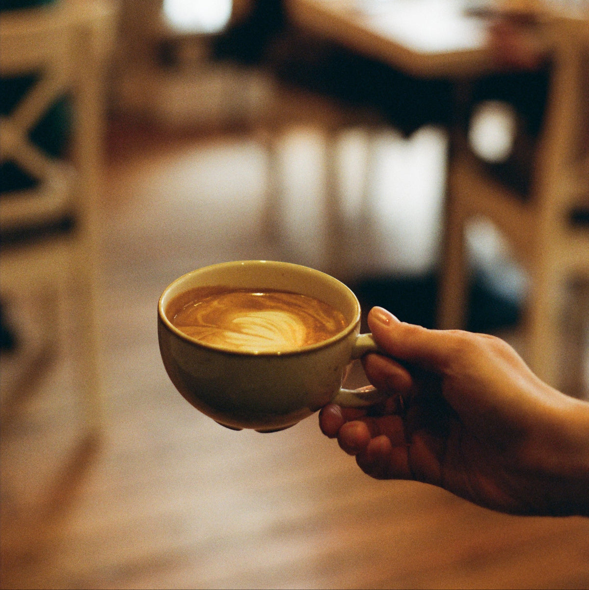 Person holding a ceramic coffee cup in a blurred indoor setting